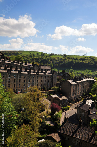 A view of the winding streets and tall stone houses in hebden bridge se in the surrounding west yorkshire countryside with pennine hills and bright summer trees with blue cloudy sky