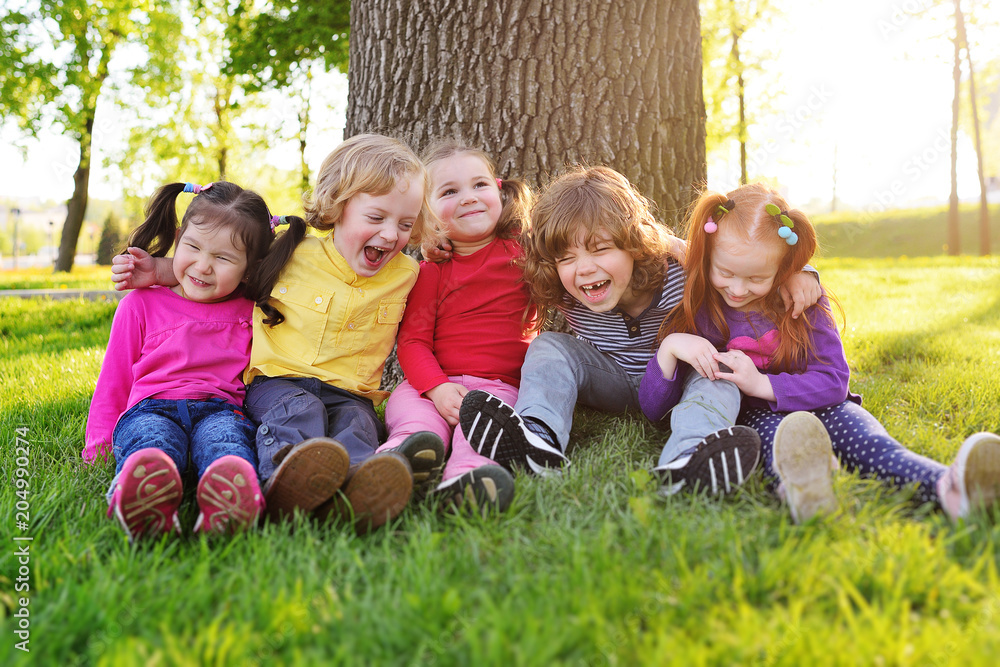 Φωτογραφία a group of small children in colorful clothes embracing sitting on the grass under a tree in a park laughing and smiling