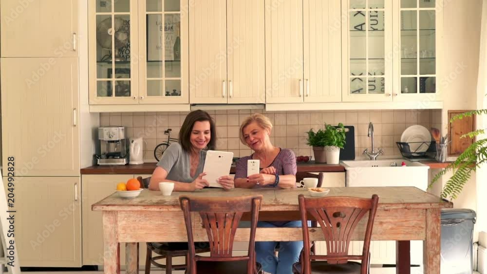 Beautiful Mother and daughter sitting with tablet and smartphone in the kitchen
Beautiful Mother and daughter sitting with tablet and smartphone in the kitchen