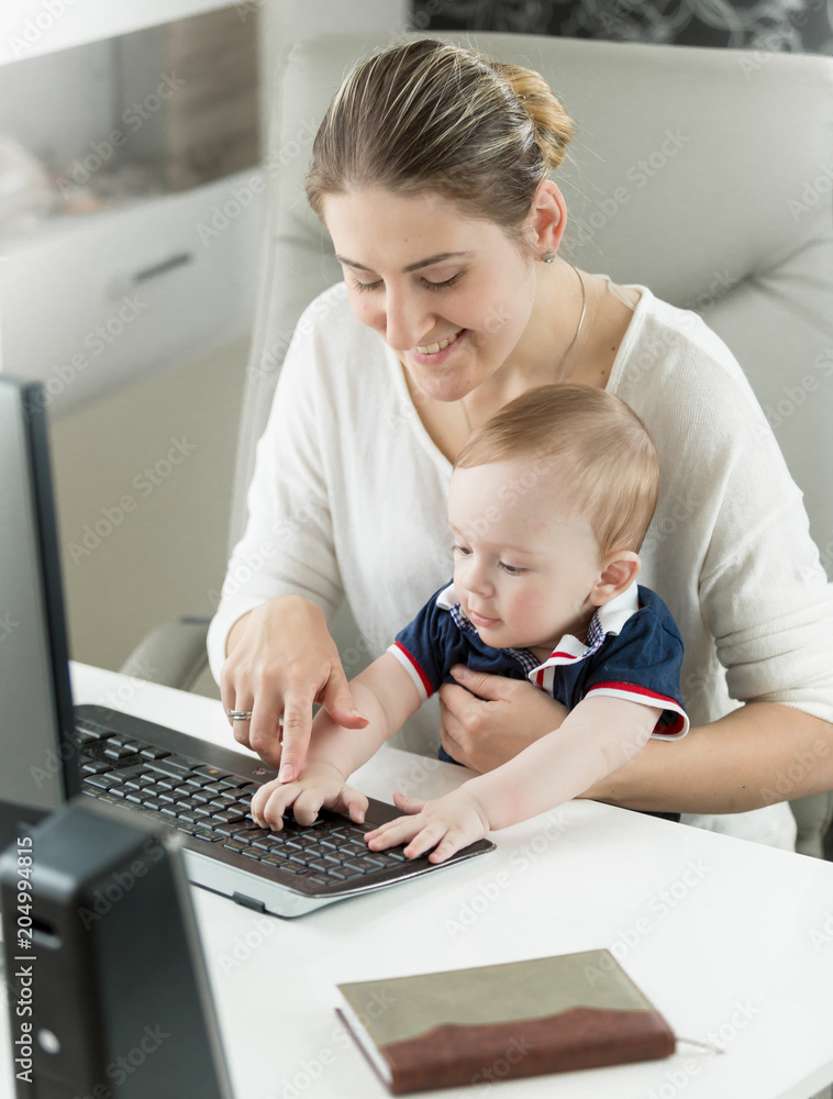 Portrait of smiling young woman teaching her baby son using computer at office Portrait of smiling young woman teaching her baby son using computer at office
