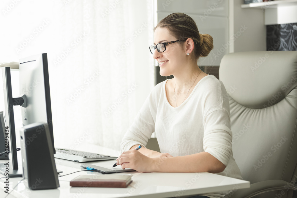 Portrait of smiling young woman in eyeglasses working in office and using graphic tablet Portrait of smiling young woman in eyeglasses working in office and using graphic tablet