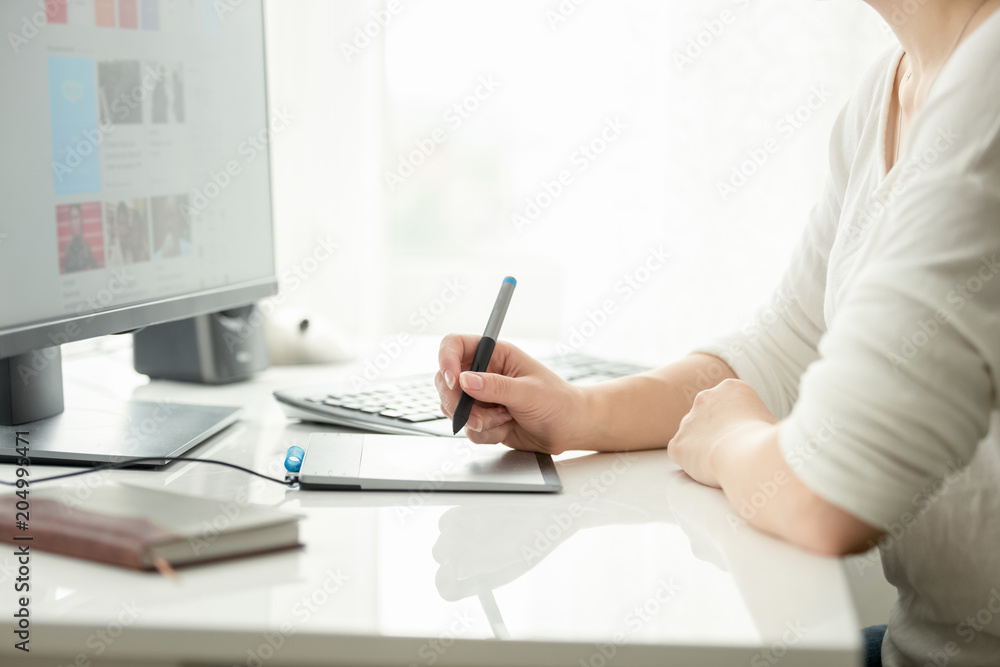 Fototapeta premium Closeup image of young female graphic designer holding stylus and working with graphic tablet