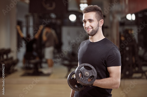one young man, ordinary average looking, one arm dumbell exercise, smirking, in gym. Unrecognizable group of people behind. photo