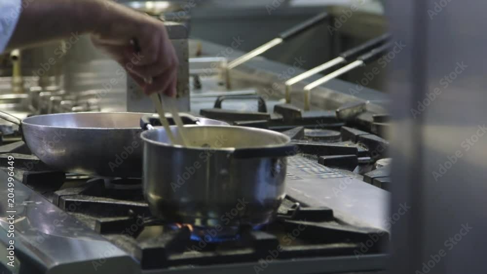 Close up, chef watches stovetop pans Close up, chef watches stovetop pans