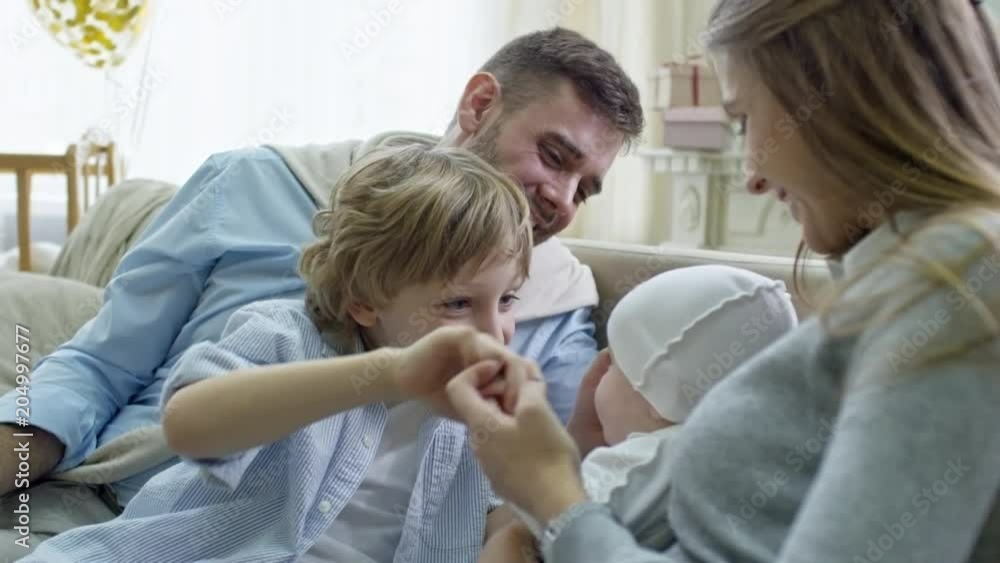 Tilt up of elementary age boy playing with baby brother while sitting with parents on sofa