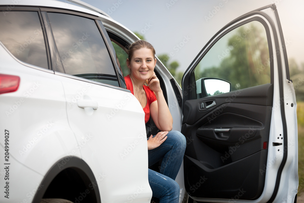 Portrait of beautiful smiling young owmna sitting on car passenger seat wuth open door