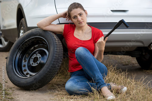 Portrait of young woman sitting at broken caar in field and holding car wheel wrench © Кирилл Рыжов