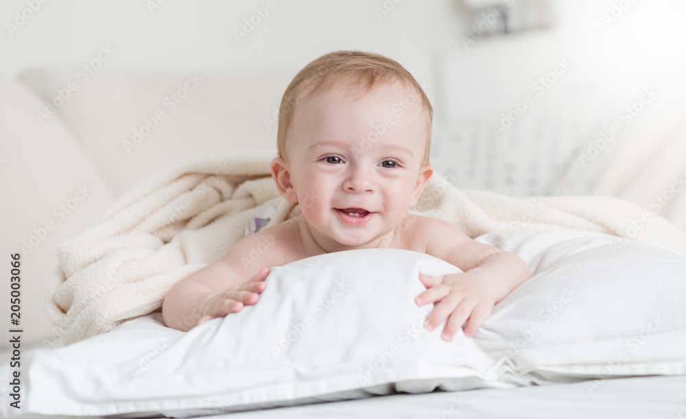 Portrait of cute smiling baby boy lying on bed on big white pillow
