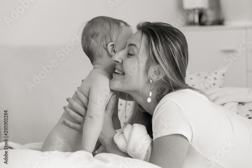 Black and white portrait of young caring mother hugging her baby son sitting on bed