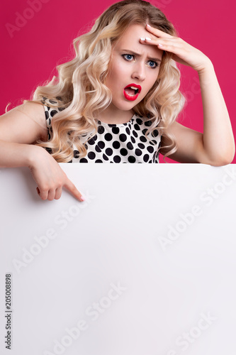 An outraged emotional girl, with blond curly hair and bright red lips, indicat on an empty white background. Place for your advertisement, presentation. photo