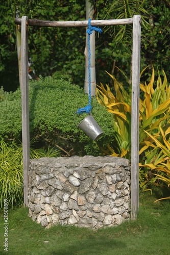 Old water well Rock water well in a garden with a metal pail hanging around it photo