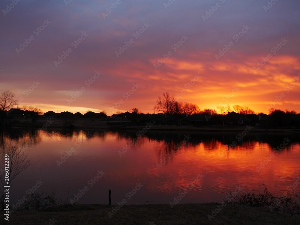 Breathtaking winter sunset Fiery skies casting reflections on a lake and the bare trees at sunset in winter