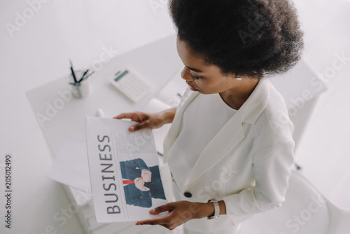 high angle view of attractive african american businesswoman reading newspaper in office