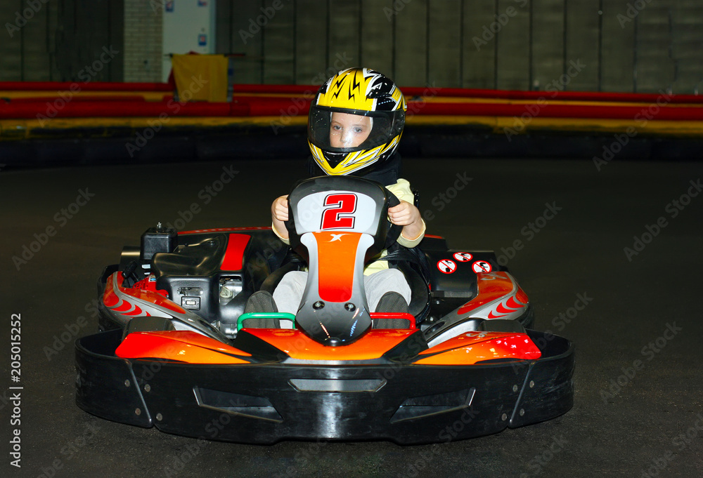 a the smiling little girl in a helmet in the go-kart on the karting track indoors