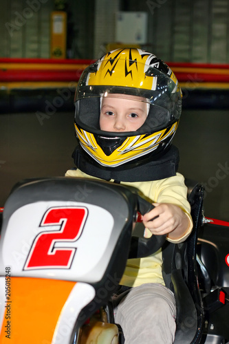 a the smiling little girl in a helmet in the go-kart on the karting track indoors © 977_rex_977
