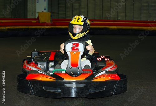 a the smiling little girl in a helmet in the go-kart on the karting track indoors