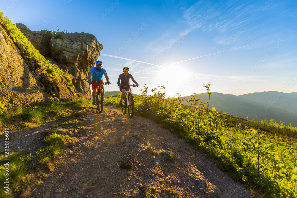 Cycling women and man riding on bikes at sunset mountains forest landscape. Couple cycling MTB enduro flow trail track. Outdoor sport activity.