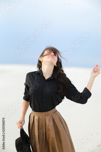 Young girl wearing black blouse and brown skirt standing in white background and keeping hat. Concept of clothes collection and vogue.