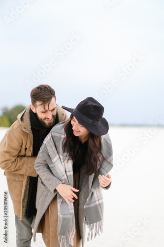 Gladden woman and man with beard wearing coats and scarfs standing in winter snow background. Concept of happy couple and positive emotions. photo