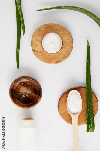 top view of organic cream in container and spoon with salt on wooden slices, aloe vera leaves and wooden bowl with aloe vera juice