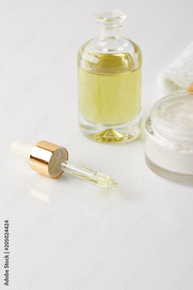 closeup view of organic cream in container, bottle of cosmetic oil, dropper and white towel closeup view of organic cream in container, bottle of cosmetic oil, dropper and white towel