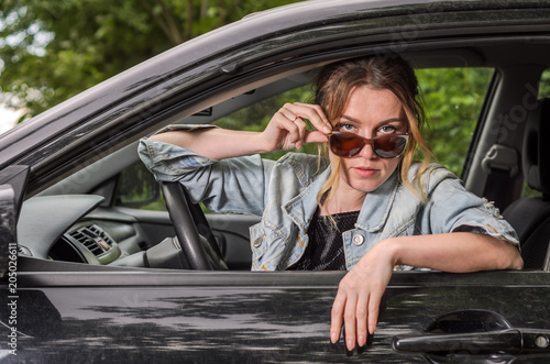 Young charming girl in sunglasses is sitting at the wheel of a car