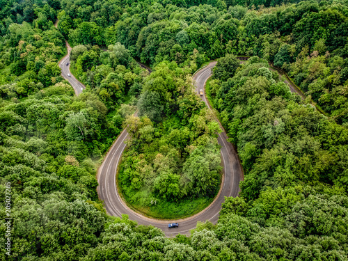 Car passing on an extreme winding road in the forest, aerial view