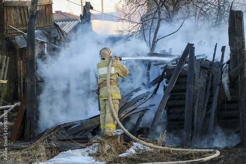 Firefighter extinguishes the fire. Fireman holding a hose with water, watering a strong stream of burning wooden structure in the smoke.
