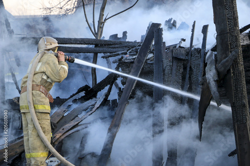 Firefighter extinguishes the fire. Fireman holding a hose with water, watering a strong stream of burning wooden structure in the smoke. photo