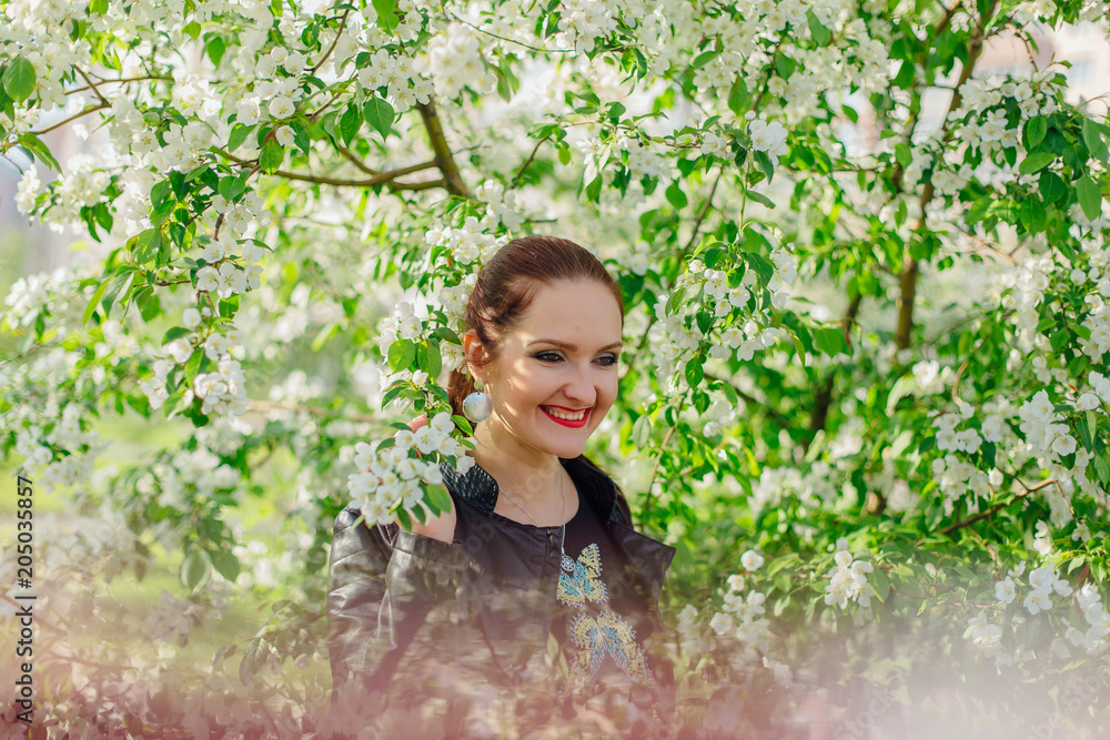 Charming woman dressed in a leather jacket under the apple tree Charming woman dressed in a leather jacket under the apple tree