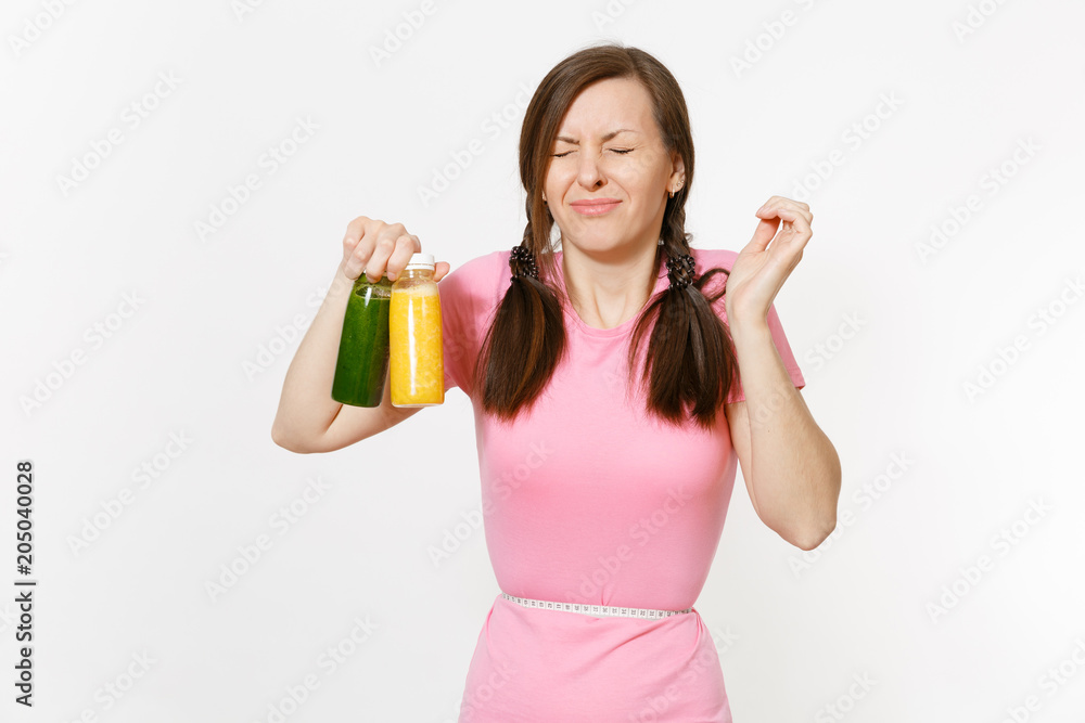 Sad woman holds green, yellow detox smoothies in bottles, measure tape on waist isolated on white background. Proper nutrition, vegetarian drink, healthy lifestyle, dieting concept. Copy space, flack. Sad woman holds green, yellow detox smoothies in bottles, measure tape on waist isolated on white background. Proper nutrition, vegetarian drink, healthy lifestyle, dieting concept. Copy space, flack.