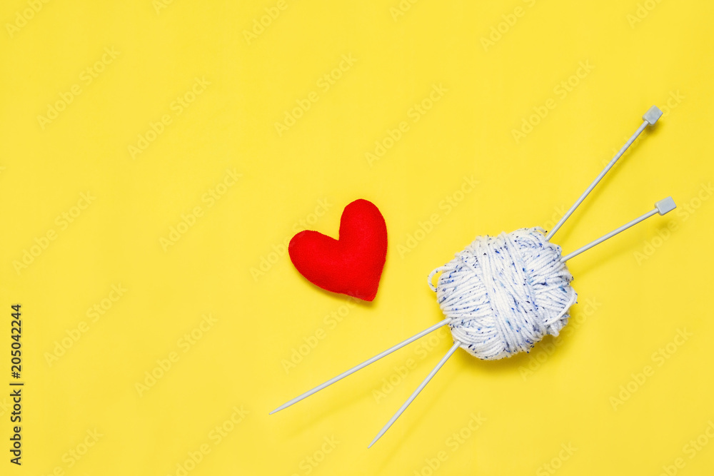 Top view of yarn and red felt heart on yellow background, love to knit image concept Top view of yarn and red felt heart on yellow background, love to knit image concept