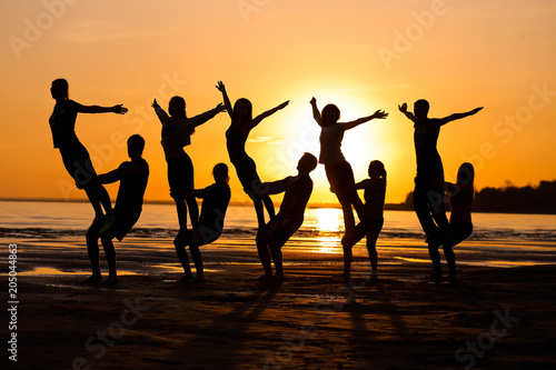 Silhouettes against the sunset are engaged in sports, fitness, yoga. A group of people.