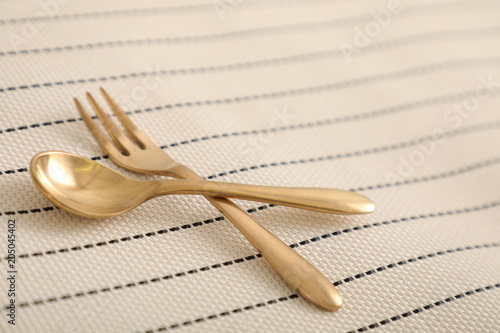淡いボーダーのテーブルクロスの上にゴールドのスプーンとフォークのランチセット　Spoon and fork lunch set on a pale border table cloth	