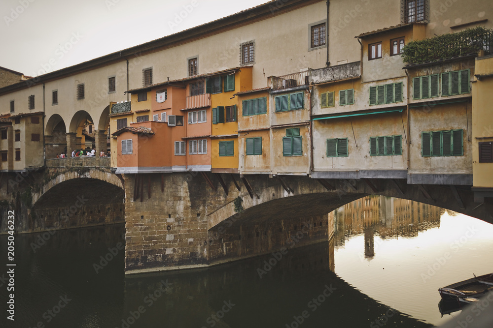 Florence, Italy. View of the Golden bridge and old houses on the waterfront of the river Arno. Cloudy sky. Houses are reflected in the water.