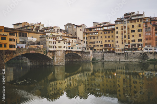 Florence  Italy. View of the Golden bridge and old houses on the waterfront of the river Arno. Cloudy sky. Houses are reflected in the water.