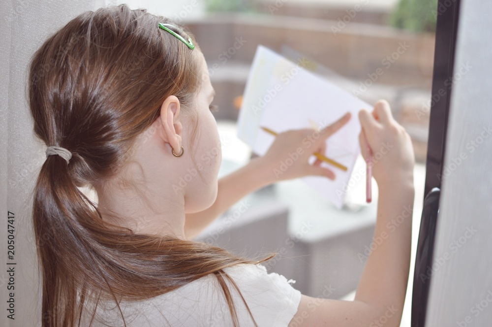 Child, girl, 8 years old, blond hair, drawing on a white sheet of paper supported on the glass, selective focus, back portrait