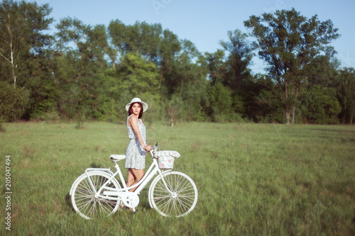 Young beautiful woman with a white bicycle in a meadow.