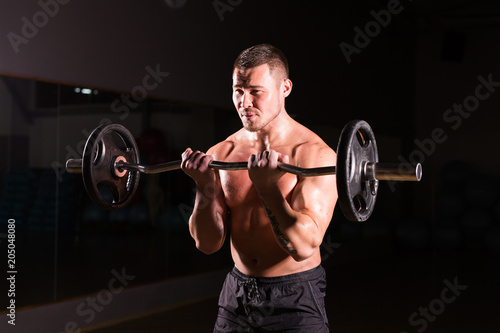 Powerful bodybuilder doing the exercises with barbell. Strong male with naked torso on dark background. Strength and motivation.