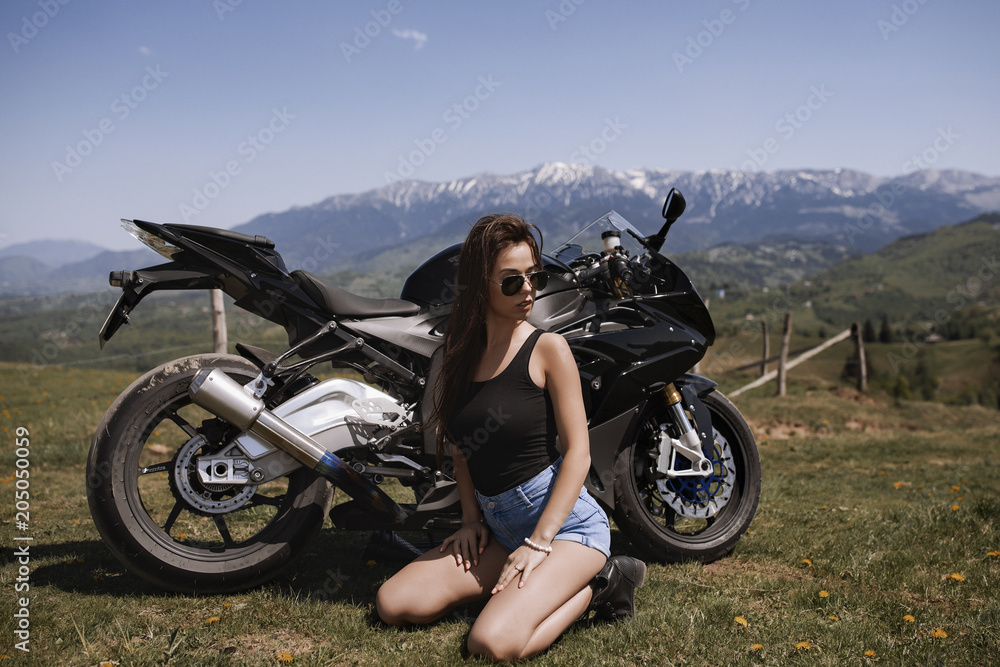 Obraz premium Beautiful woman posing with a motorcycle in mountain scenery