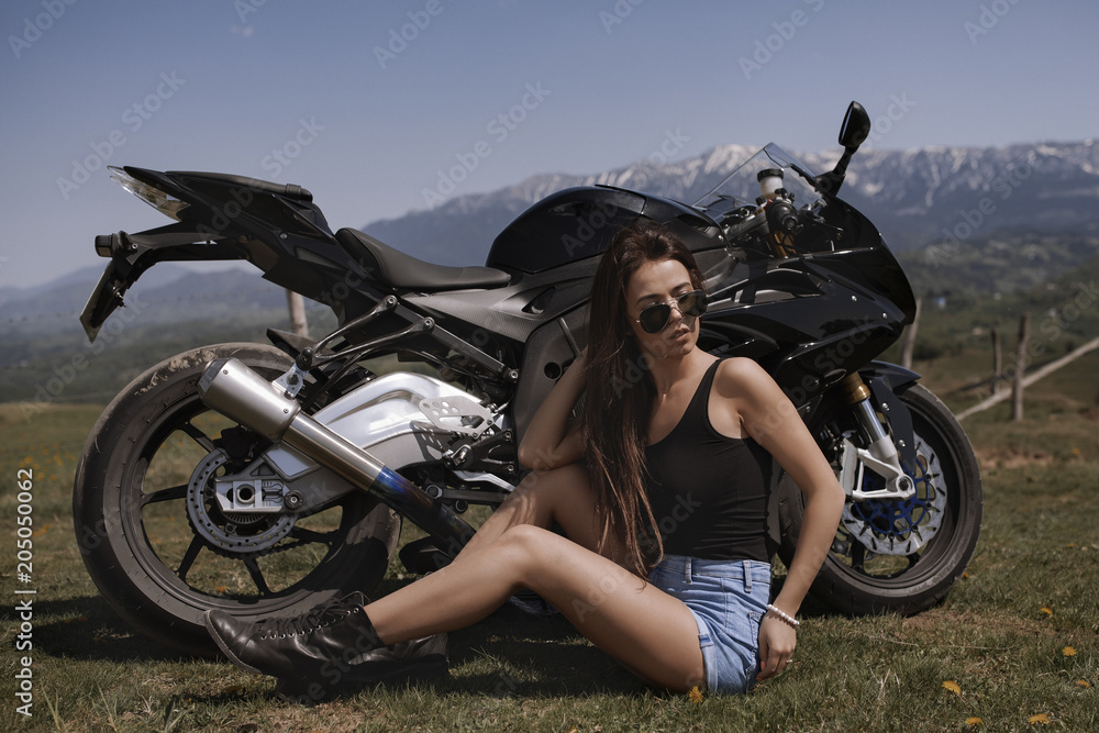 Obraz premium Beautiful woman posing with a motorcycle in mountain scenery