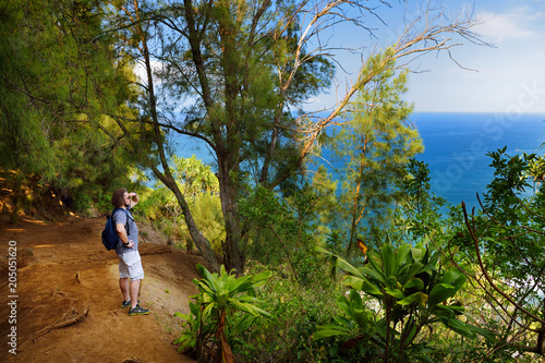 Young male tourist hiking on beautiful Pololu loop trail located near Kapaau, Hawaii, that features beautiful wild flowers and stunning views to the Pololu Valley