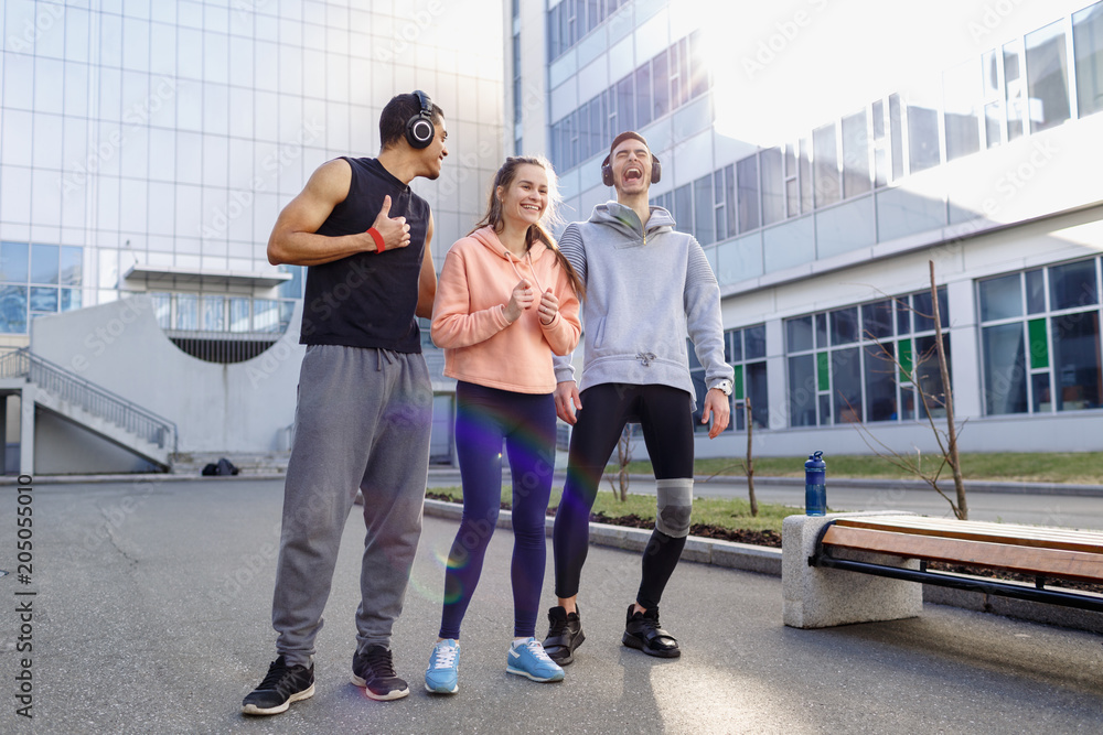 Fototapeta premium Young people go in for sports in the city. Rest after training. Guys in headphones are doing sports in the city.