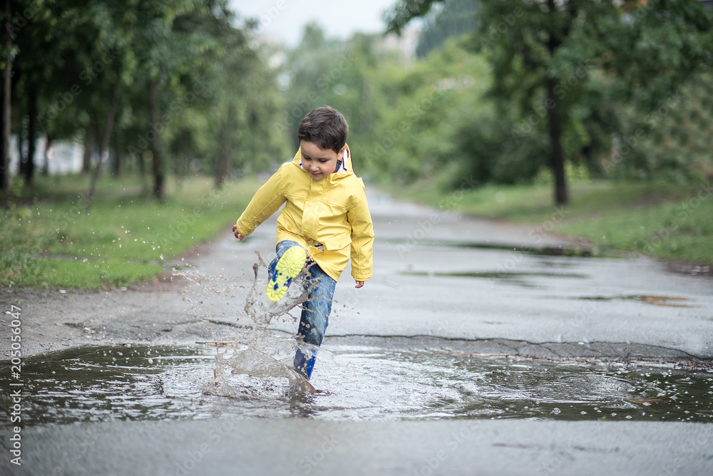 A wet child is jumping in a puddle. Fun on the street. Tempering in summer