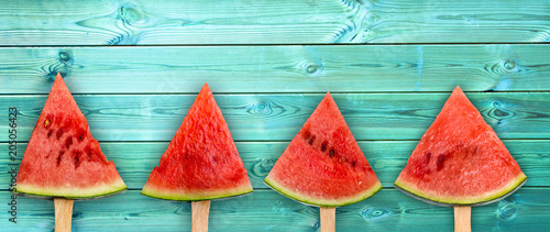 Four watermelon slice popsicles on panoramic blue wood background, fresh summer fruit concept