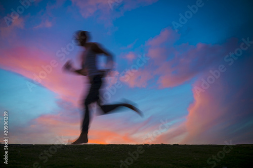 Colorful sunset view of a silhouette of a man running with motion blur. Slow shutter speed to enhance sense of movement.