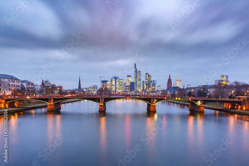 Picturesque view of Frankfurt am Main skyline and Ignatz Bubis Brucke bridge during evening blue hour with mirror reflections in the river, Germany © Kavalenkava