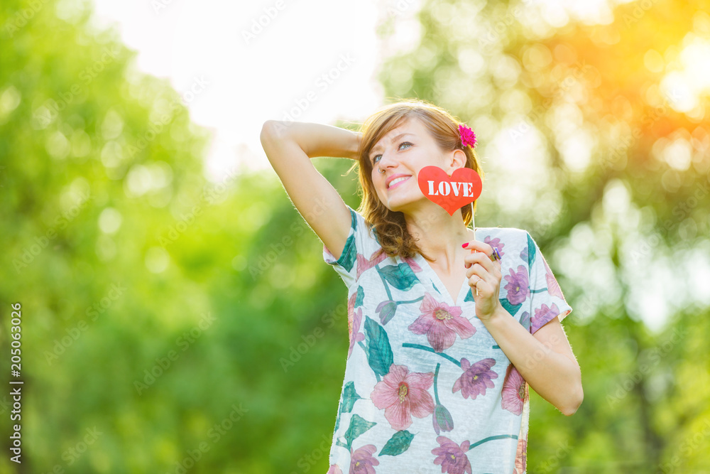 Cute young woman holding a paper heart - shaped sign outdoors. Cute young woman holding a paper heart - shaped sign outdoors.