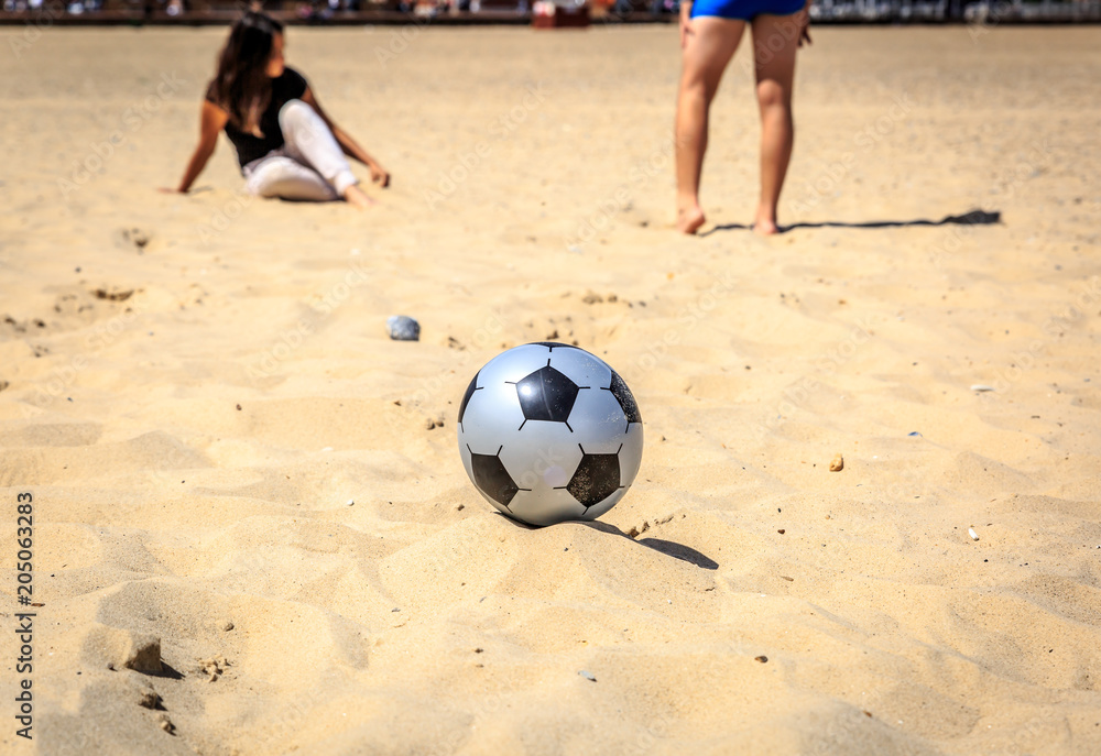Close-up of a football ball near a girl and a boy, on a quiet beach