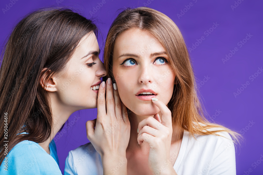 Two pretty women gossipping with face reaction expression before blue background Two pretty women gossipping with face reaction expression before blue background